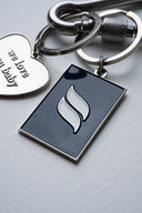 Silver metal keychain with polished finish, deep-blue tag engraved with Sleeves Studios icon, silver heart on back stamped “We love you, baby,” designed as a meaningful accessory