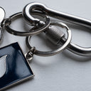 Silver metal keychain with polished finish, deep-blue tag engraved with Sleeves Studios icon, silver heart on back stamped “We love you, baby,” designed as a meaningful accessory