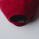 Red corduroy cap with soft ribbed texture, curved “Sleeves Studios” front embroidery, brand icon below, SLV initials on the side, structured crown and adjustable back for custom fit