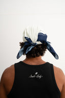 Person wearing a black tank top with 'smile Baby' branding, standing against a white background.  white and blue bandanna / headscarf with text "Wrap it with confidence baby"  and "Sleeves Studios" branding