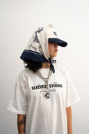 Person wearing a white t-shirt with text, navy cap, and headscarf on a plain background -  white and blue bandanna / headscarf with text "Wrap it with confidence baby"  and "Sleeves Studios" branding