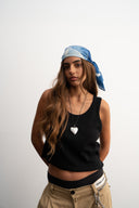 Woman wearing a black tank top, beige pants, and a blue headscarf on a white background - blue bandanna / headscarf  with text "tie your style baby"