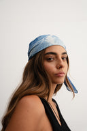 Woman wearing a blue patterned headscarf against a white  -  blue bandanna / headscarf  with text "tie your style baby"background