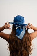 Person wearing a blue headscarf with white patterns on a plain background - blue bandanna / headscarf  with text "tie your style baby"background
