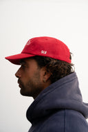 Red corduroy cap with soft ribbed texture, curved “Sleeves Studios” front embroidery, brand icon below, SLV initials on the side, structured crown and adjustable back for custom fit
