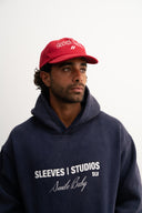 Red corduroy cap with soft ribbed texture, curved “Sleeves Studios” front embroidery, brand icon below, SLV initials on the side, structured crown and adjustable back for custom fit