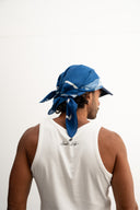 Person wearing a blue bandana and white tank top on a plain background - blue bandanna / headscarf  with text "tie your style baby" Sleeves Studios' branding