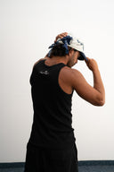 Person wearing a black tank top and cap with a bandana, standing against a plain background -  white and blue bandanna / headscarf with text "Wrap it with confidence baby"  and "Sleeves Studios" branding