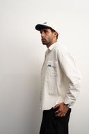 Man wearing a white shirt and blue white cap against a plain background - sleeves studios - white Button-up shirt - blue label - white shirt