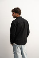 Man wearing a black jacket and light blue jeans against a white - background - sleeves studios - black Button-up shirt - blue label 