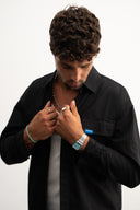 Man adjusting his collar against a plain background - sleeves studios - black Button-up shirt - blue label 