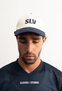 white and blue cotton cap, lightweight and breathable, SLV initials embroidered above the visor, Sleeves Studios icon on back, adjustable strap for one-size fit