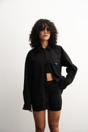 Person wearing a black oversized shirt with a small blue logo on a white background - sleeves studios - black Button-up shirt - blue label 