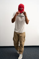 Person wearing a red beanie, white t-shirt, and beige cargo pants on a plain background