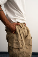 Khaki cotton baggy pants with high-waisted street fit, elastic back waistband, side and back pockets, zipper fly, and relaxed drape for everyday comfort by Sleeves Studios