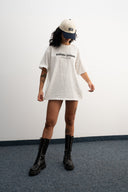 Person wearing a white oversized t-shirt, black boots, and a cap on a plain background