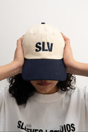white and blue cotton cap, lightweight and breathable, SLV initials embroidered above the visor, Sleeves Studios icon on back, adjustable strap for one-size fit