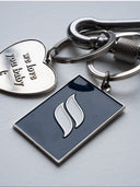 Silver metal keychain with polished finish, deep-blue tag engraved with Sleeves Studios icon, silver heart on back stamped “We love you, baby,” designed as a meaningful accessory
